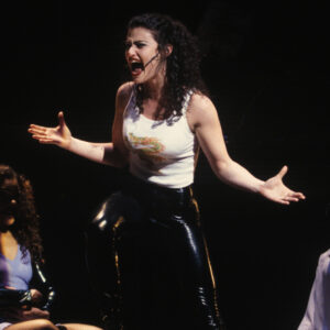 A young woman with dark curly hair singing on stage.